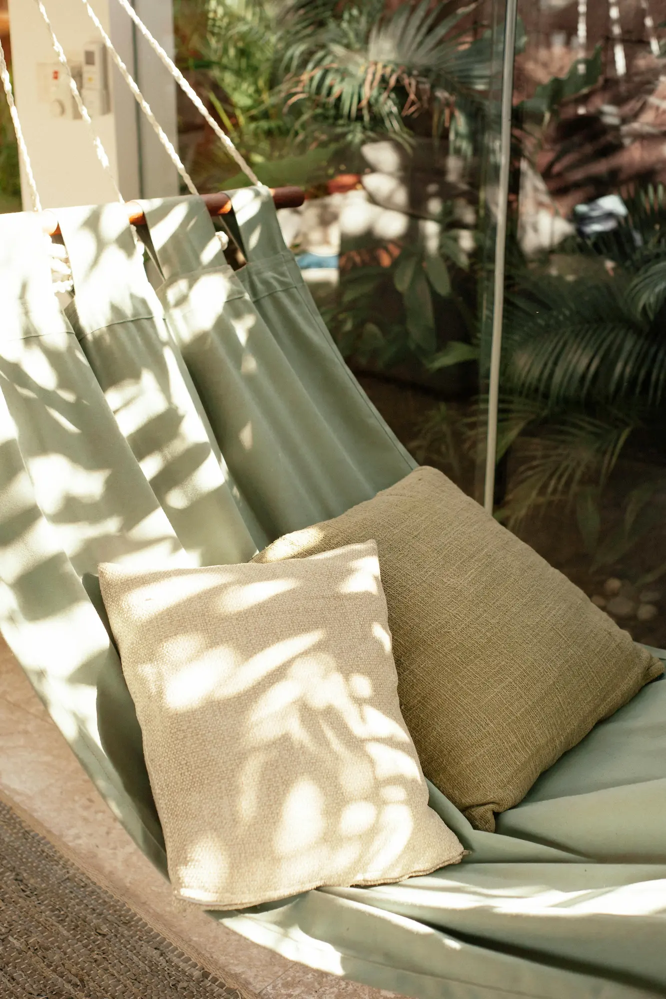 A simple cotton hammock with pillows hanging in a peaceful Mediterranean garden with a stone wall with home insurance in Mallorca.